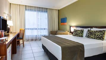 A hotel room with a bed, a desk, a chair, a television, and a window with curtains.