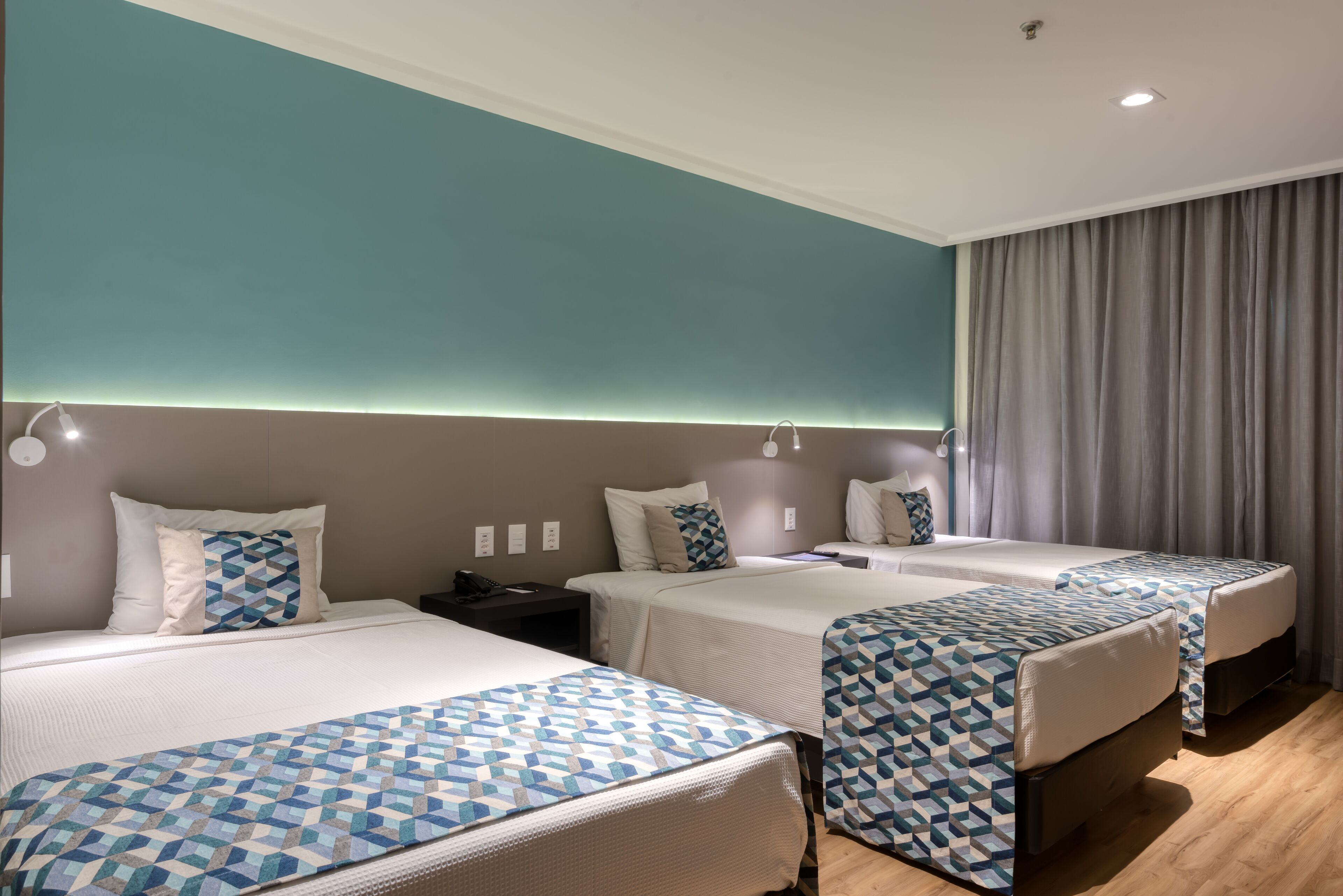 Habitación de hotel con tres camas, cada una con una colcha estampada, una mesita de noche y una lámpara.