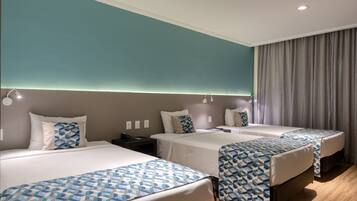 Habitación de hotel con tres camas, cada una con una colcha estampada, una mesita de noche y una lámpara.