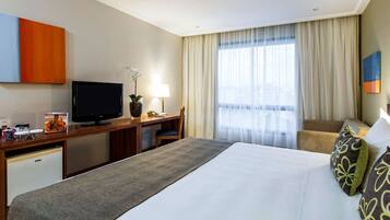 Habitación de hotel con una cama grande, un escritorio con ordenador, televisor y un refrigerador pequeño.