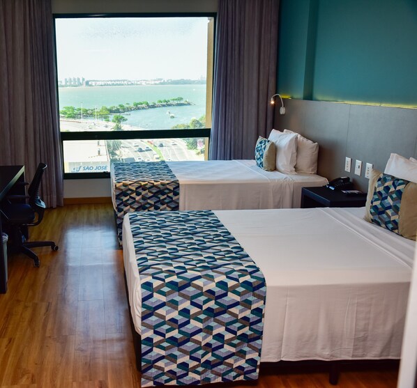 A hotel room with two beds, a desk, and a view of a body of water. - Comfort Suites Vitoria (Vitoria)