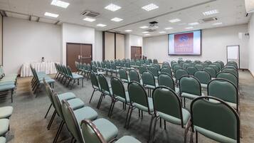 Un salón de conferencias con hileras de sillas verdes, una pantalla de proyección que muestra 'Comfort Suites' y piso alfombrado.