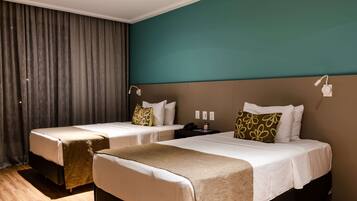 Habitación de hotel con dos camas, un ventanal con cortinas, una pared de acento color aguamarina y piso de madera.