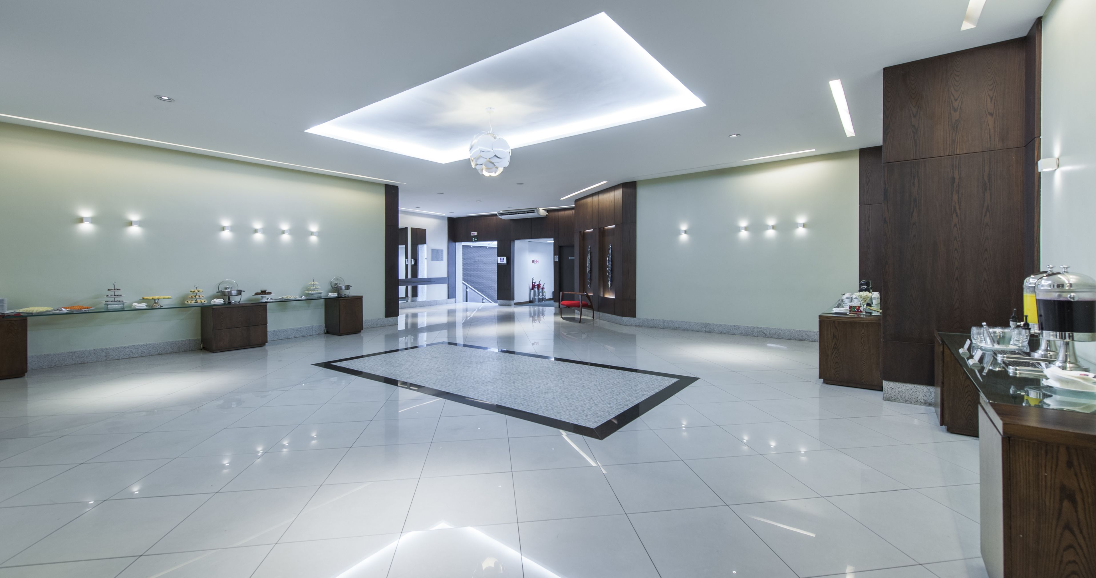 A spacious lobby with a modern design, featuring a central area rug, a reception desk, and a staircase leading to other floors.