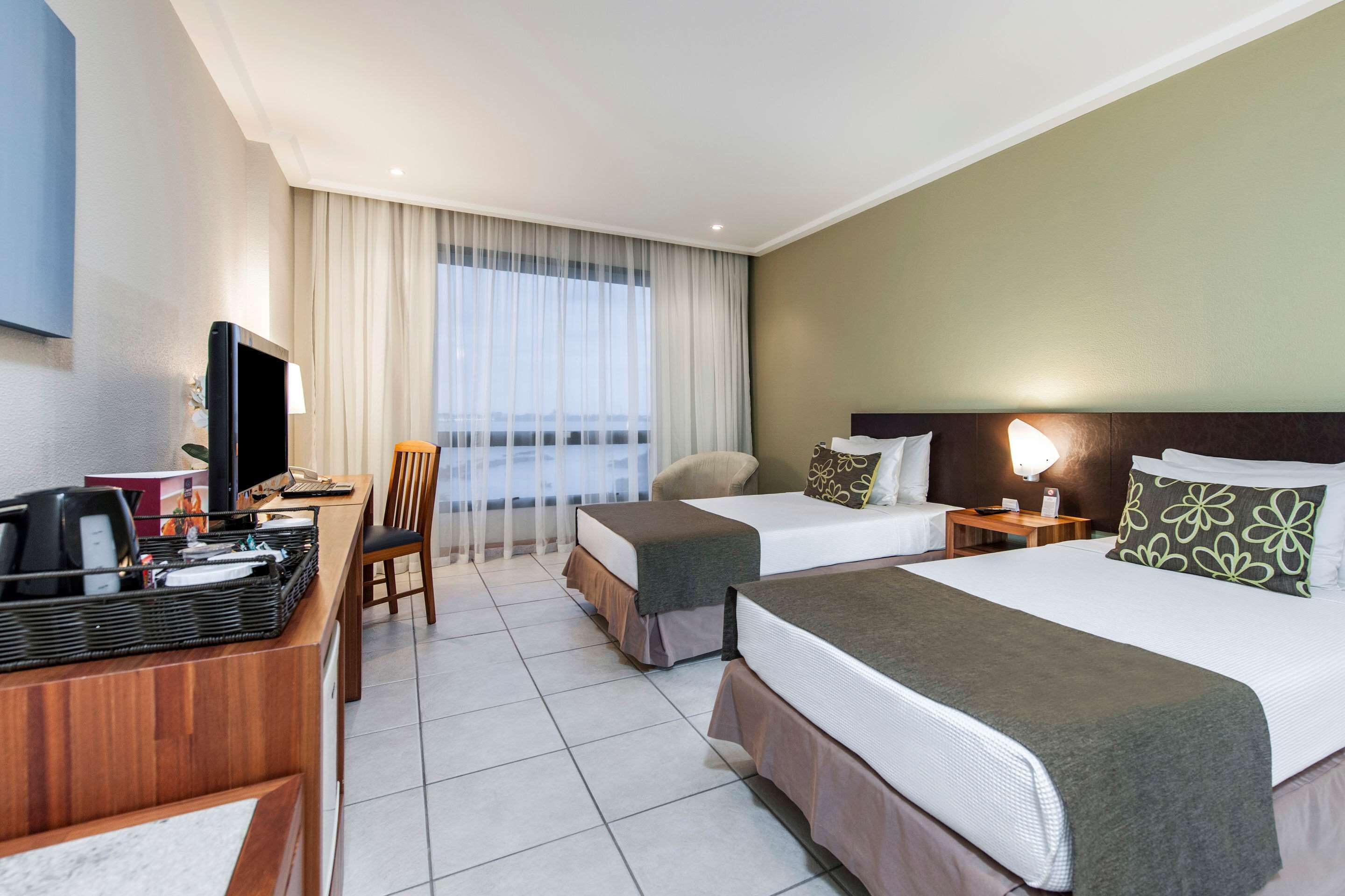 A hotel room with two beds, a desk with a computer, a TV, and a window with curtains.