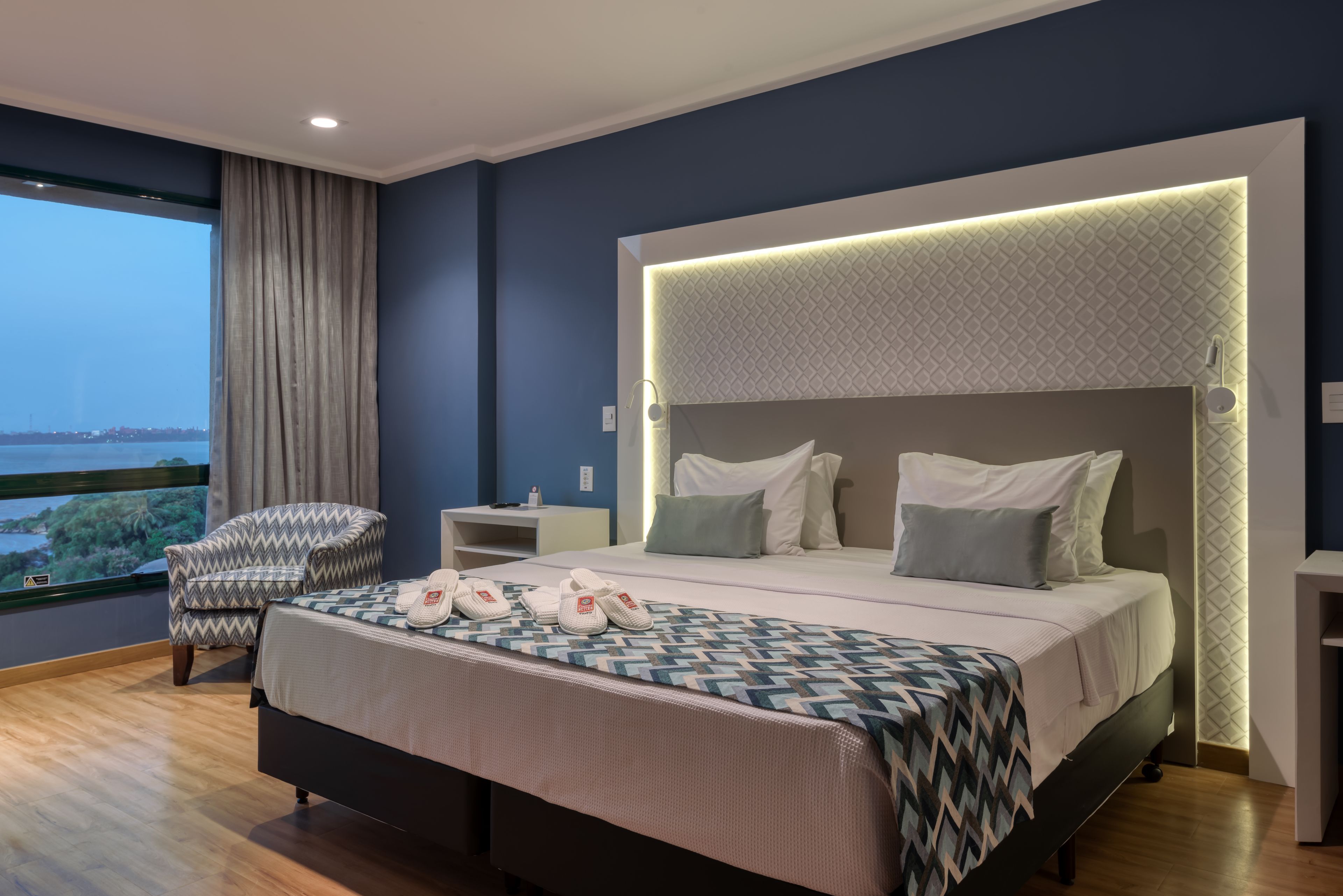 Une chambre d’hôtel moderne avec un grand lit, une chaise, une table de chevet et une vue sur la ville.
