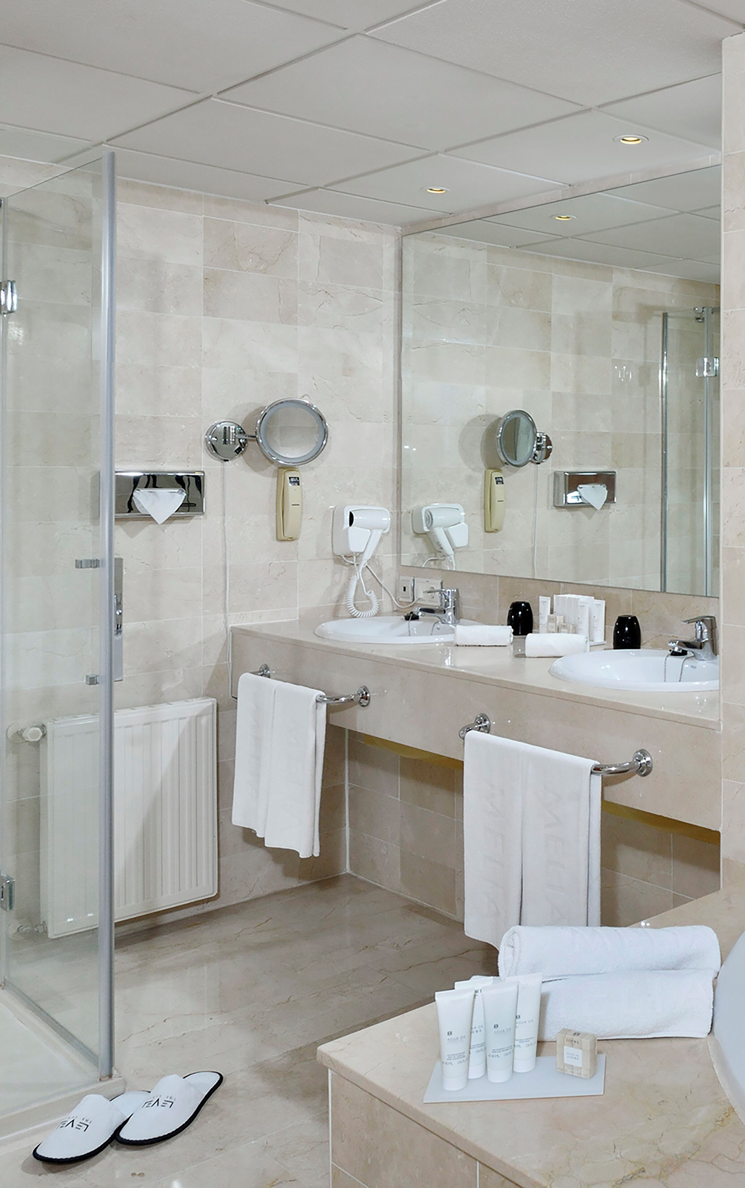 Un baño moderno con dos lavamanos, cabina de ducha de vidrio y tocador con artículos de aseo.