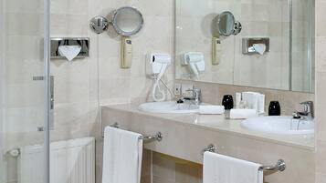 Un baño moderno con dos lavamanos, cabina de ducha de vidrio y tocador con artículos de aseo.