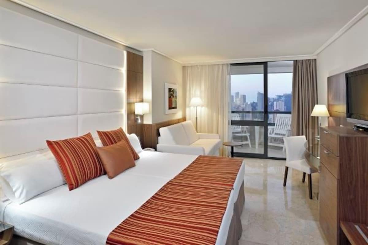 Une chambre d’hôtel avec un grand lit, une télévision, un bureau et un balcon offrant une vue sur la ville.