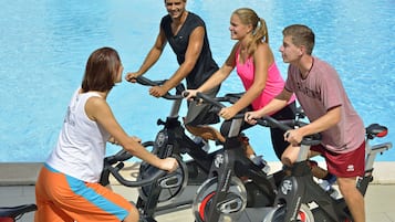 Four people using stationary bikes by a pool.