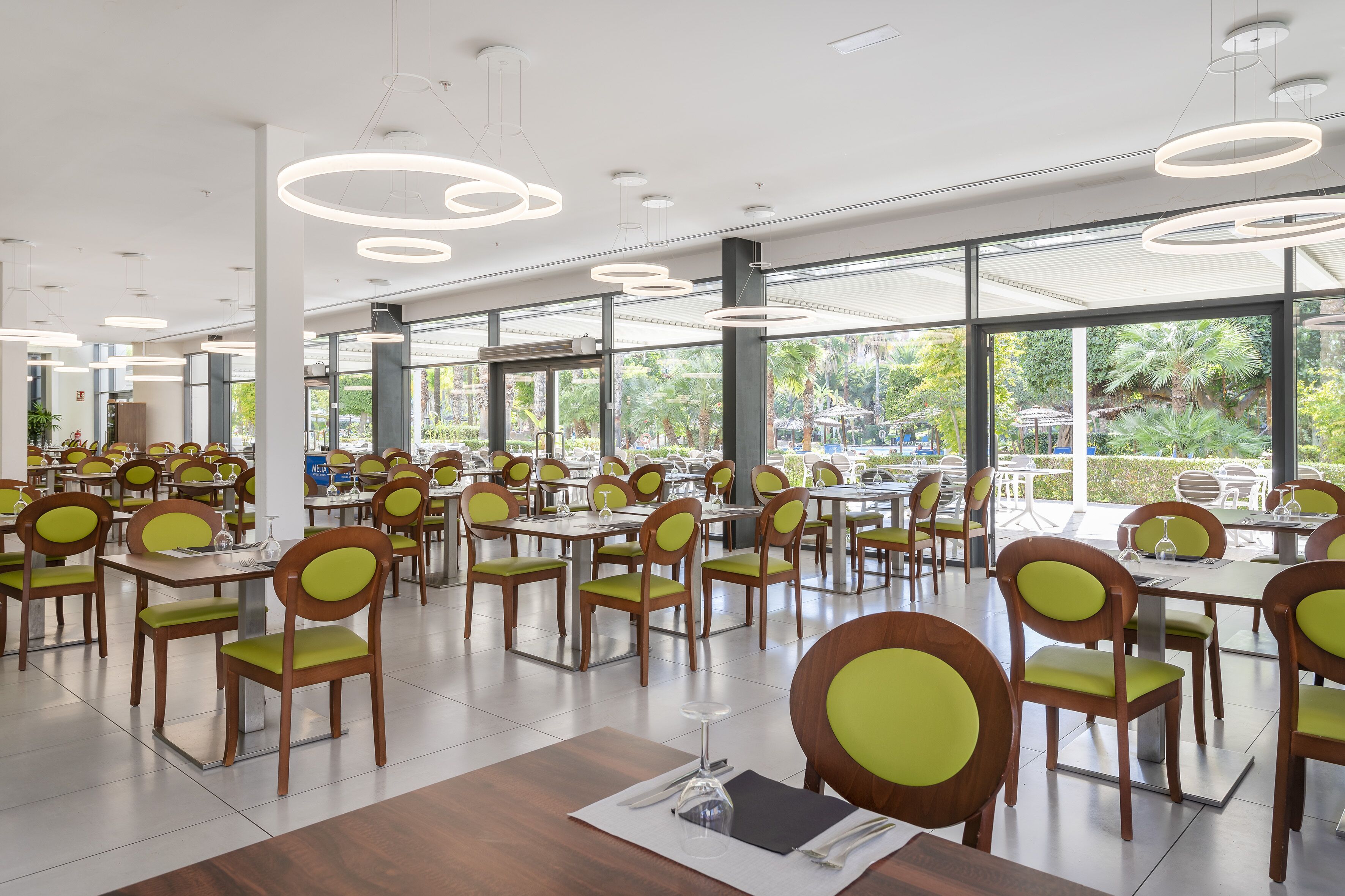 Ein geräumiges Restaurant mit mehreren Tischen und Stühlen, großen Fenstern mit Blick ins Freie und moderner Pendelleuchten.