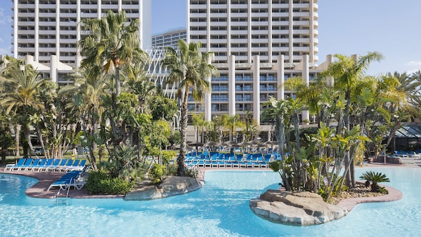 A hotel pool area with multiple water features, palm trees, and blue lounge chairs. - Melia Benidorm (Benidorm)