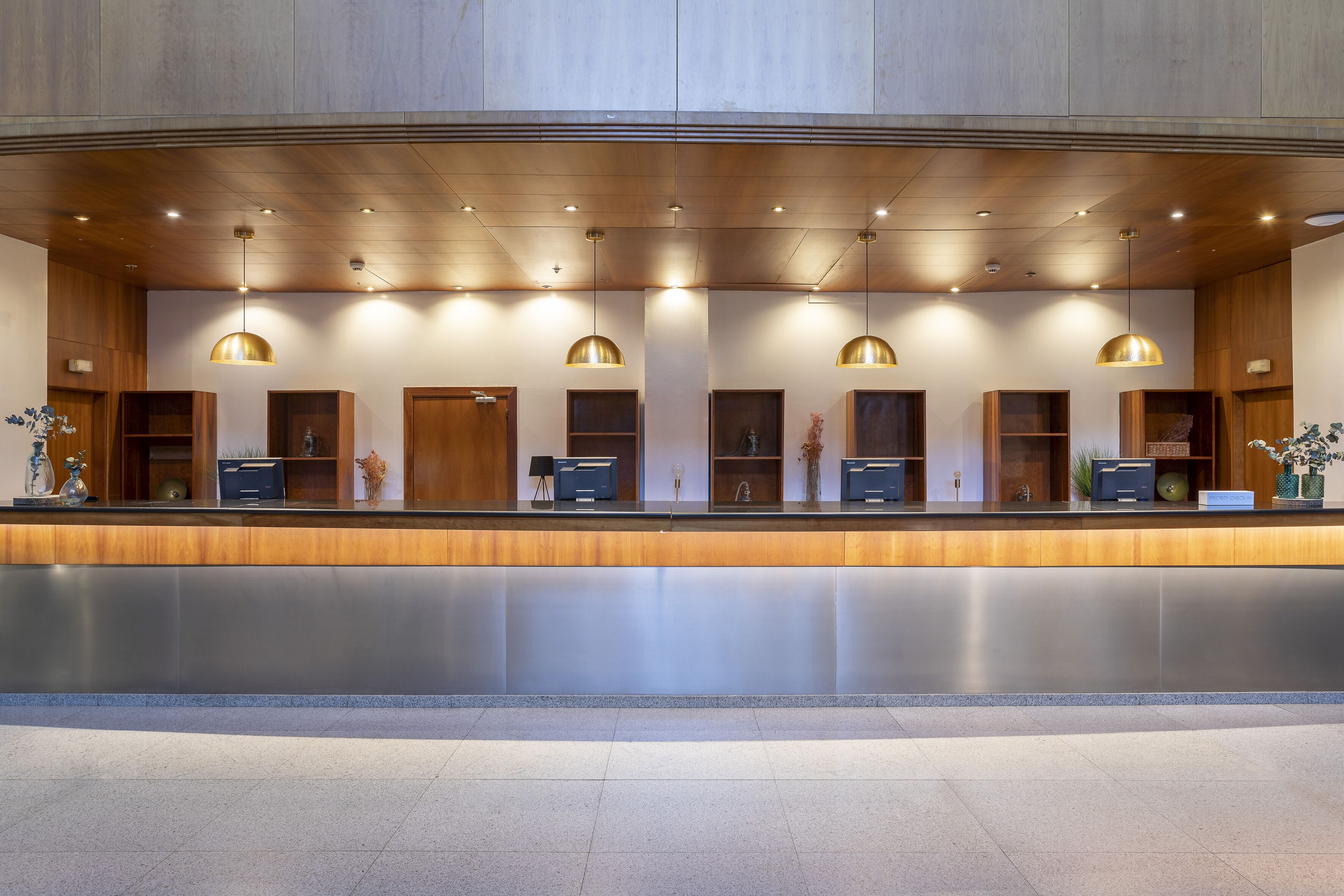 A modern hotel reception area with a long counter, wooden paneling, and pendant lighting.