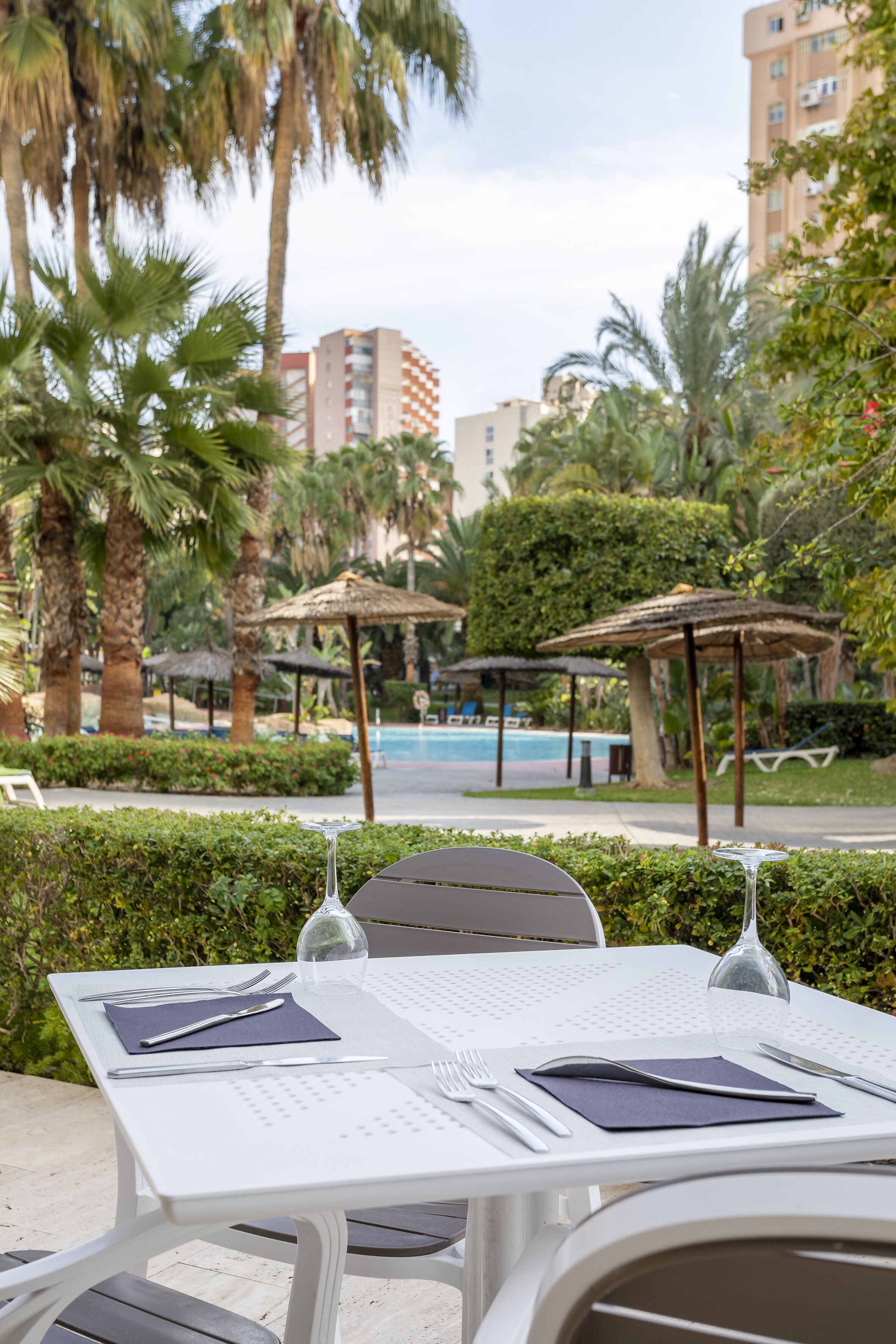 Mesa lista para comer al aire libre con vista a una piscina y palmeras.