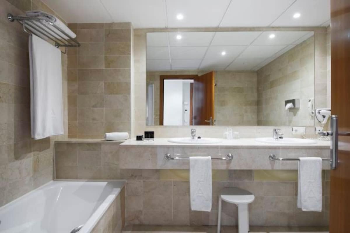 A modern bathroom with two sinks, a bathtub, a small stool, and a large mirror.