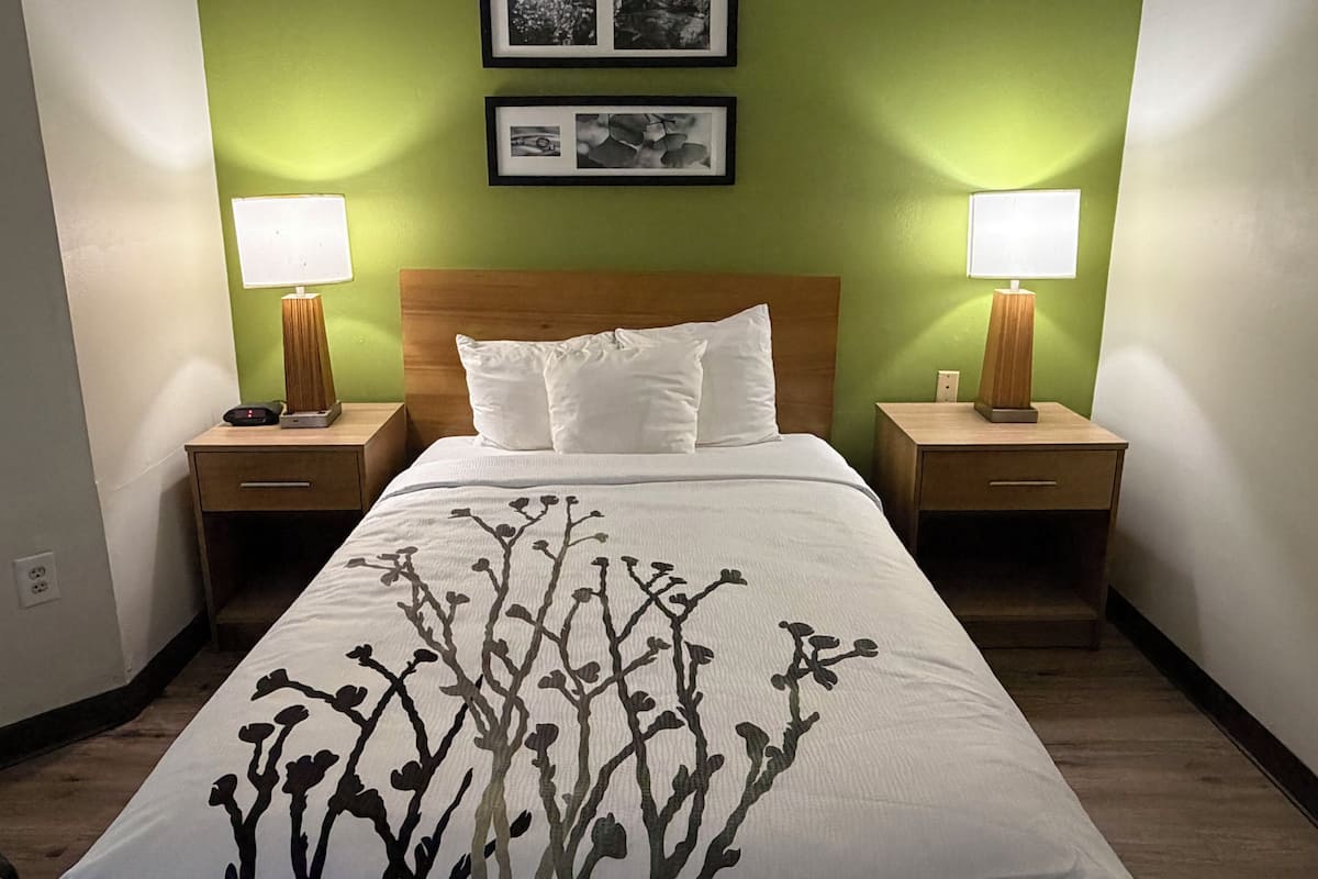 A hotel room with a bed, two bedside tables, two lamps, and two framed pictures on the wall.