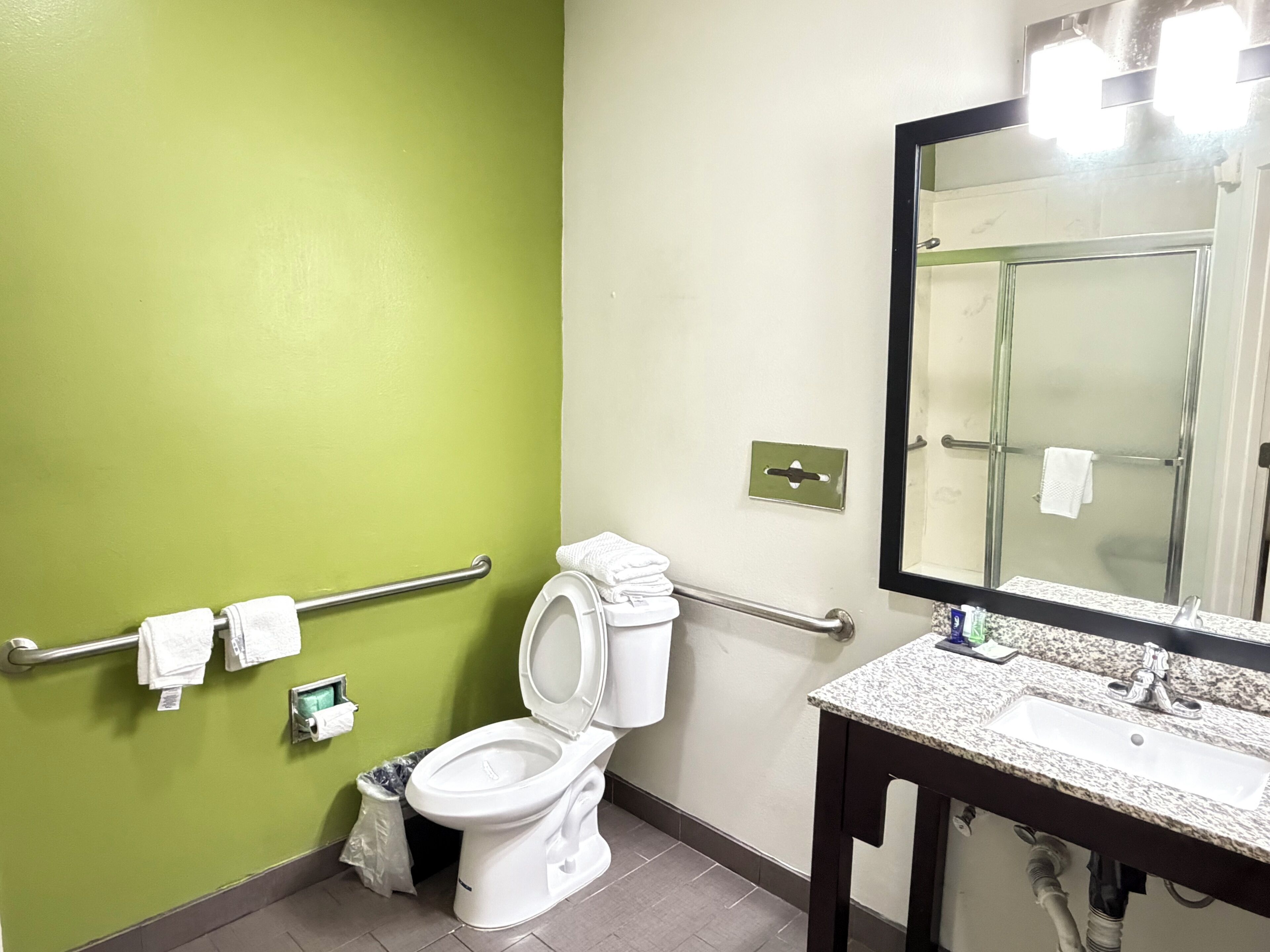 A bathroom with a green wall, white toilet, and a granite countertop sink with a mirror above.
