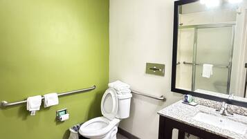 Un baño con pared verde, inodoro blanco y lavabo de granito con espejo arriba.