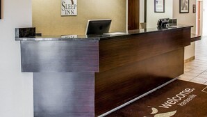 Tauleller de recepció a Sleep Inn amb disseny modern, un portàtil i un certificat emmarcat a la paret.