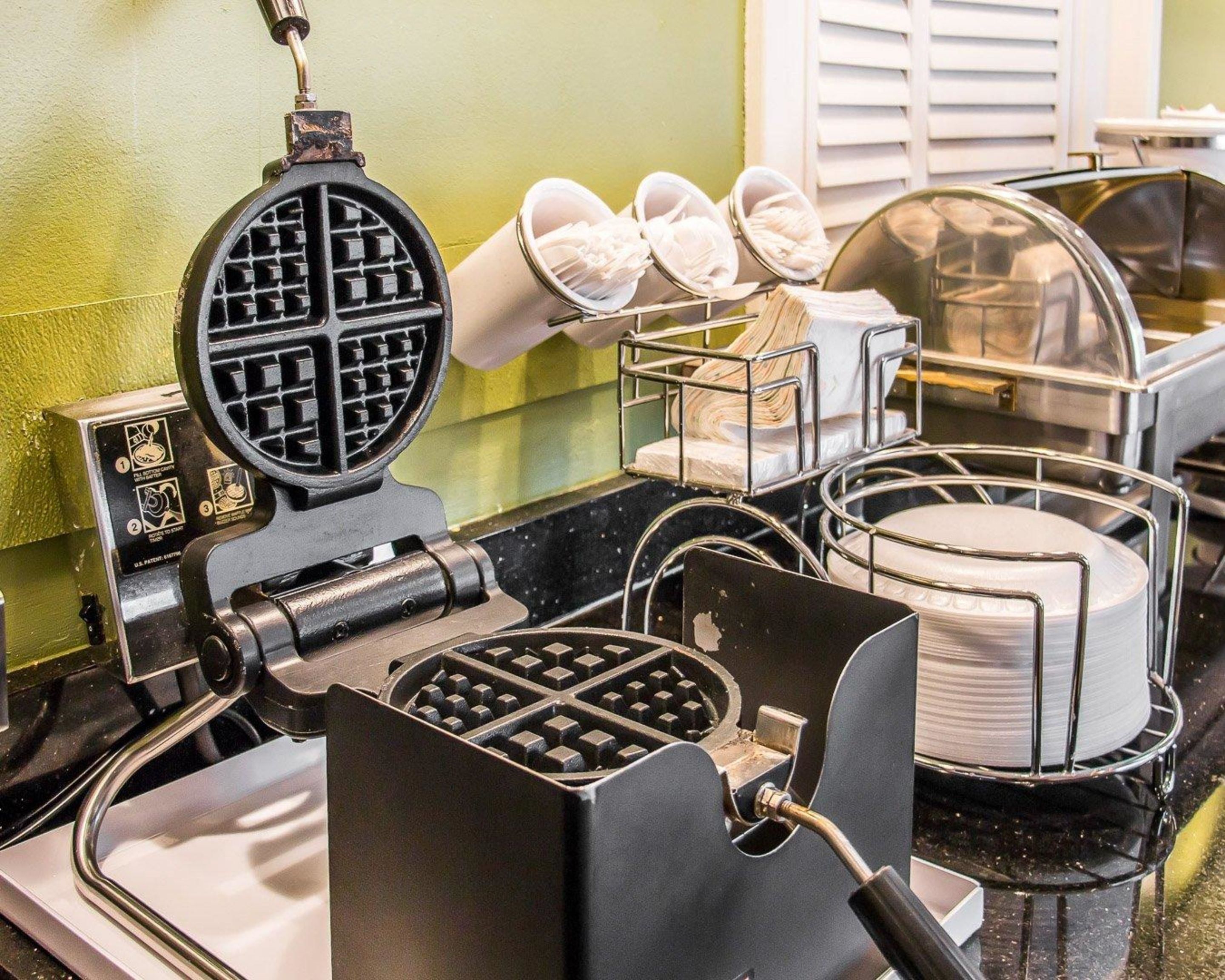 A waffle iron with a grid pattern, a stack of white paper towels, and a metal rack with white bowls.