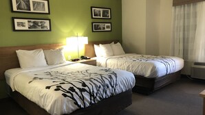 Una habitació d'hotel amb dos llits, una tauleta de nit amb una làmpada i quadres amb marc a la paret.