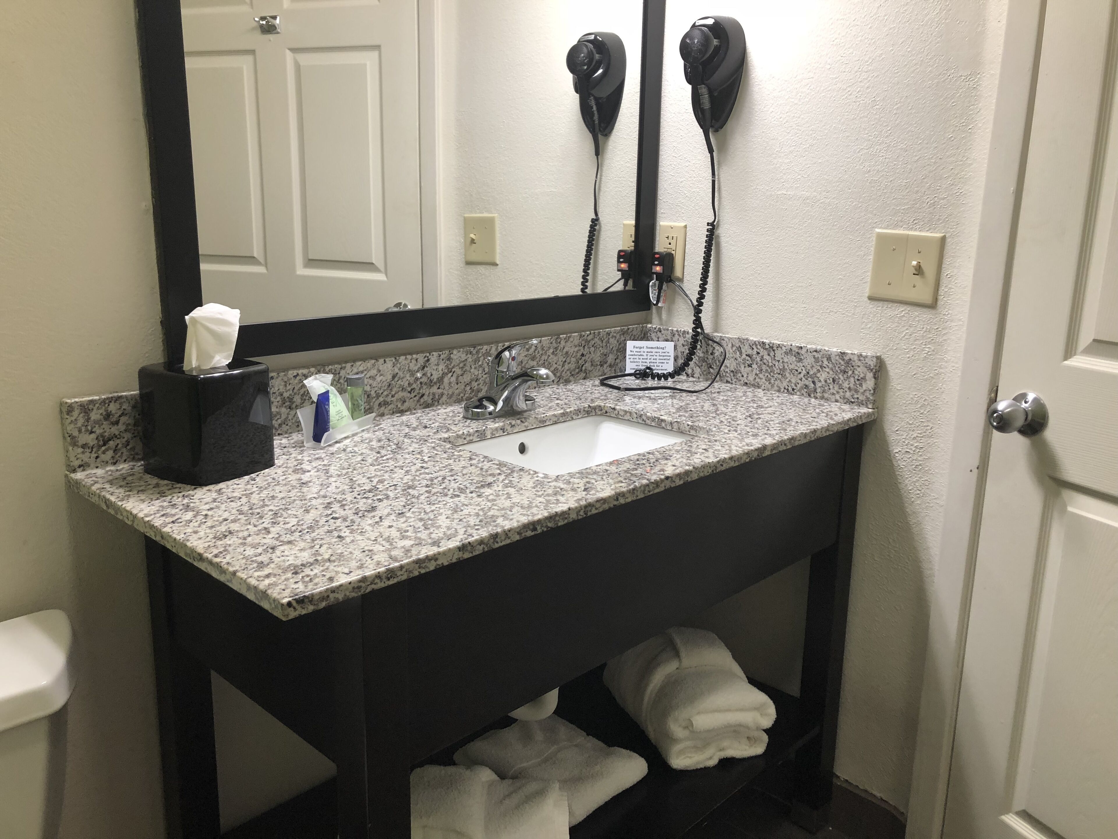A bathroom with a granite countertop sink, a mirror, a towel rack, and a hairdryer mounted on the wall.