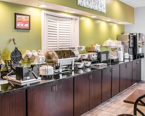 A buffet setup with various food stations, including a waffle maker, bowls, and a coffee machine.