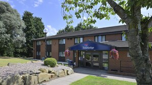 Un hôtel Travelodge avec une façade en briques, une entrée couverte et un parterre aménagé devant l’entrée.