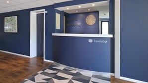 Un comptoir d’accueil avec une horloge, une pancarte indiquant « Bonjour et bienvenue » et le logo « Travelodge ».
