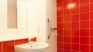 A bathroom with a white sink, a mirror, and red tiled walls. - Travelodge London Balham (London)