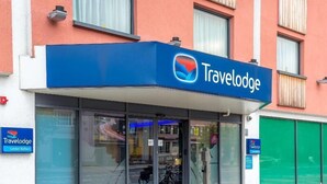 A Travelodge hotel with a blue sign, large windows, and a motorcycle parked outside. - Travelodge London Balham (London)