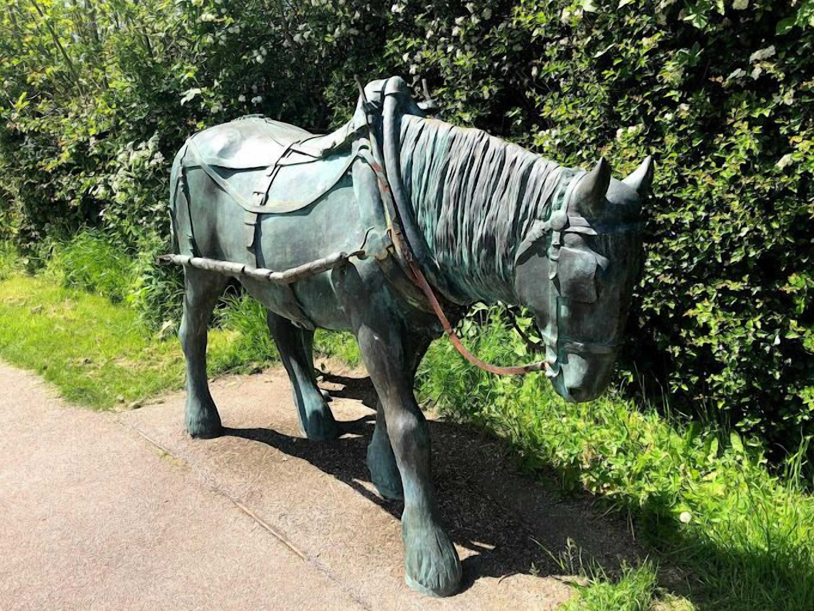 Une statue de bronze représentant une charrette tirée par un cheval, placée sur un chemin pavé.
