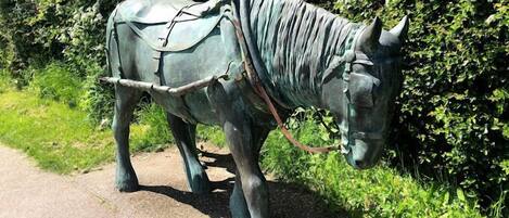Une statue de bronze représentant une charrette tirée par un cheval, placée sur un chemin pavé.