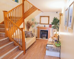Una escalera de madera que conduce a una sala de estar con chimenea, un sofá y una mesa de centro con objetos decorativos.
