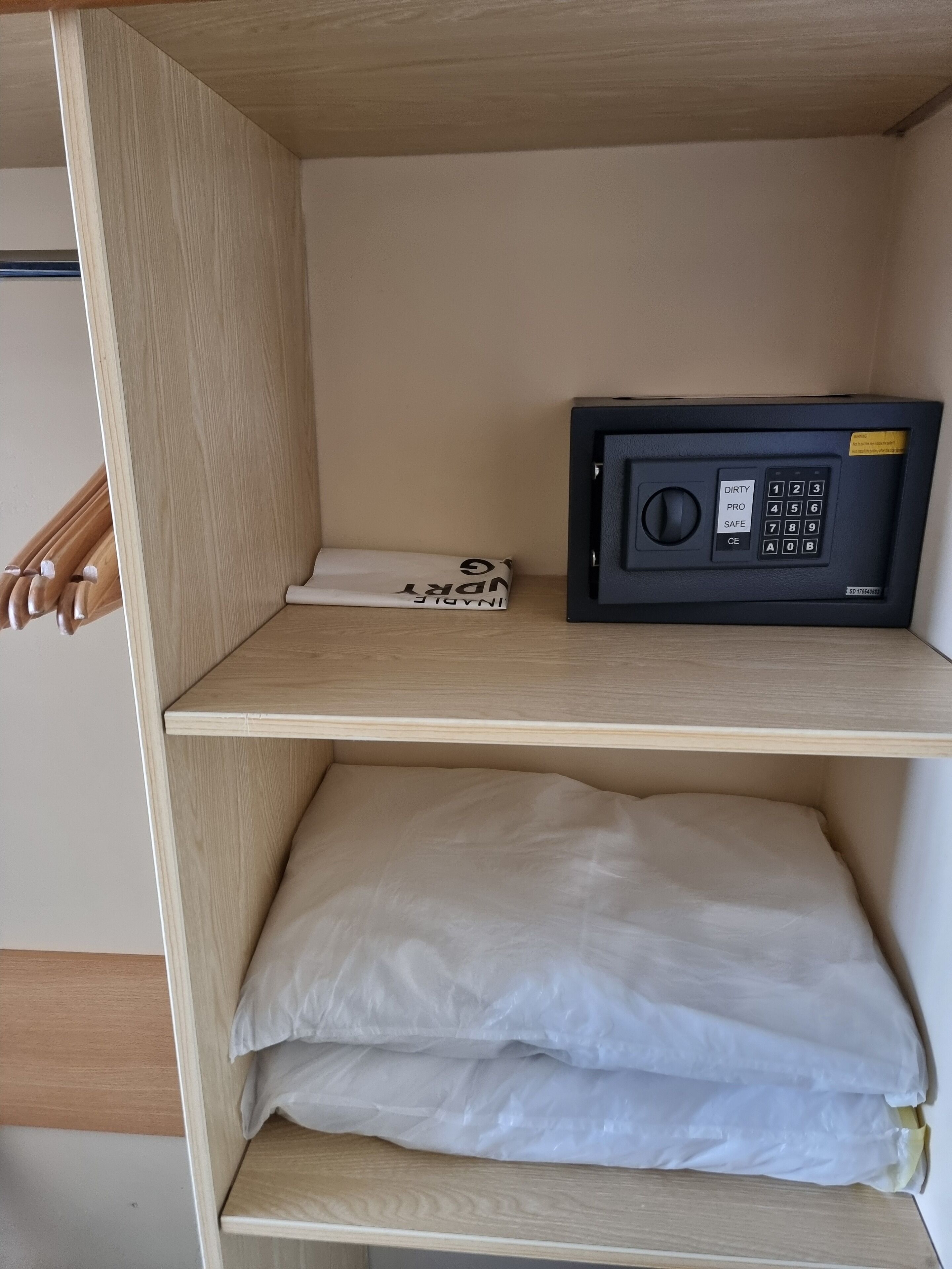 Habitación de hotel con estante de madera, caja fuerte negra y almohada blanca.