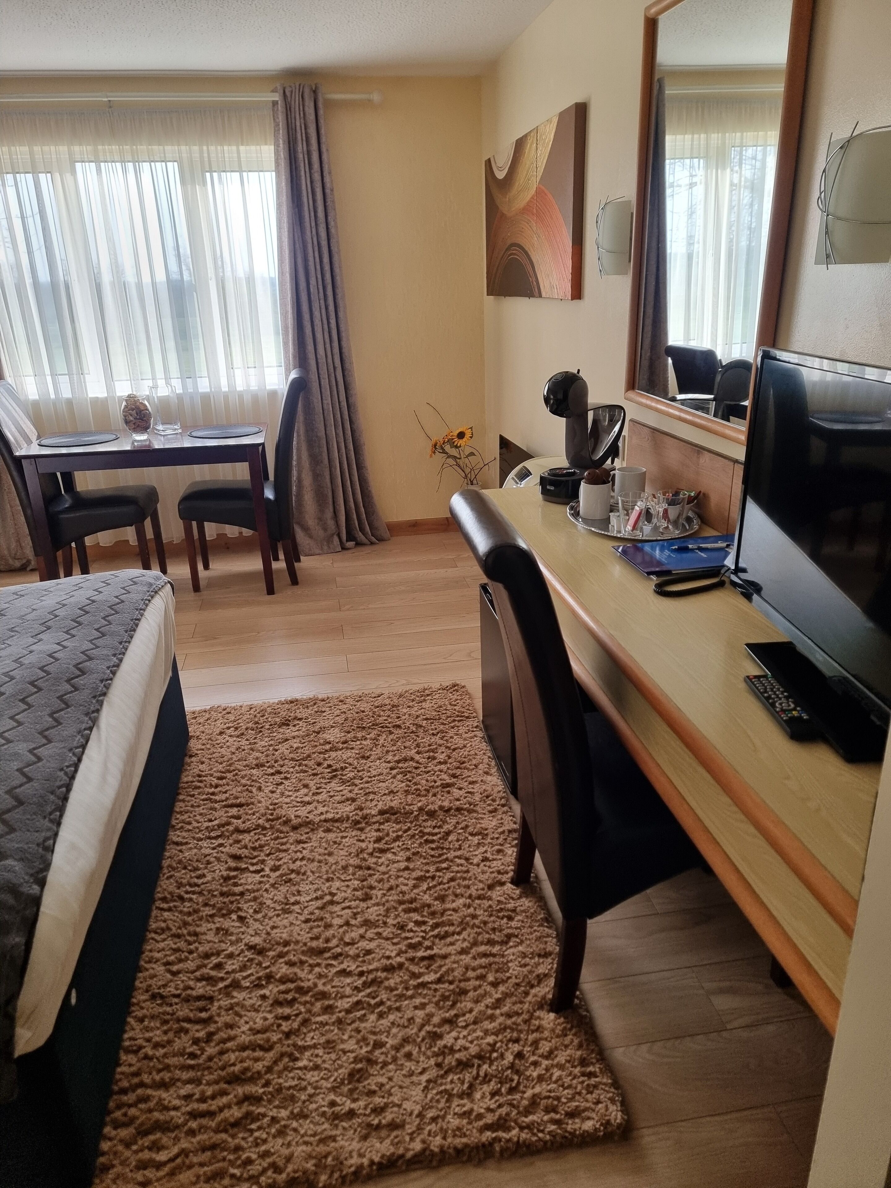 A hotel room with a bed, a desk, a chair, a coffee maker, a TV, and a window with curtains.