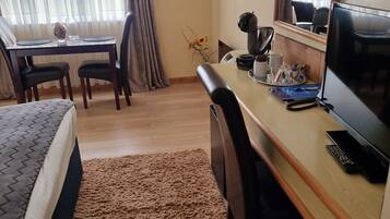 A hotel room with a bed, a desk, a chair, a coffee maker, a TV, and a window with curtains.
