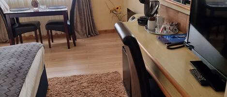 Une chambre d’hôtel équipée d’un lit, d’un bureau, d’une chaise, d’une machine à café, d’une télévision et d’une fenêtre avec des rideaux.