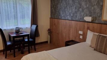 A hotel room with a bed, a desk with a chair, a vase with flowers, and a window with curtains.