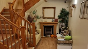 A wooden staircase leading to a living room with a fireplace, a sofa, and a side table with decorative items. - Travel Plaza Hotel (Kettering)