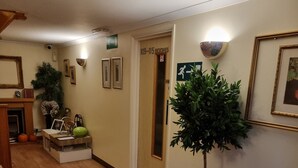 A hallway with wooden flooring, a potted plant, a framed picture, and a door with a sign. - Travel Plaza Hotel (Kettering)