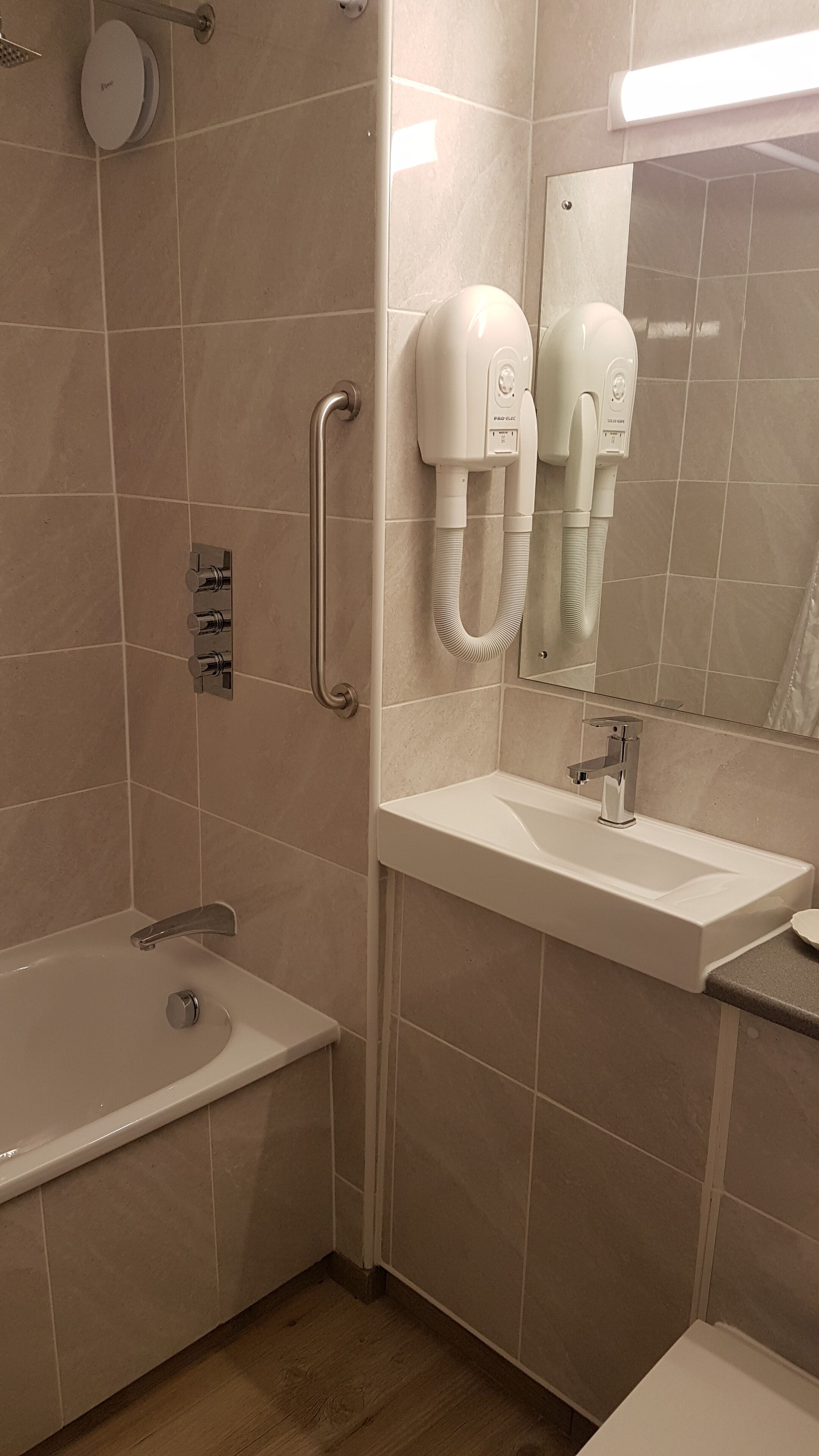 Un baño con bañera, lavamanos y dos secadores de pelo fijados a la pared.