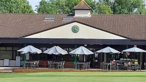 A building with a clock, outdoor seating with umbrellas, and a green lawn. - Travel Plaza Hotel (Kettering)