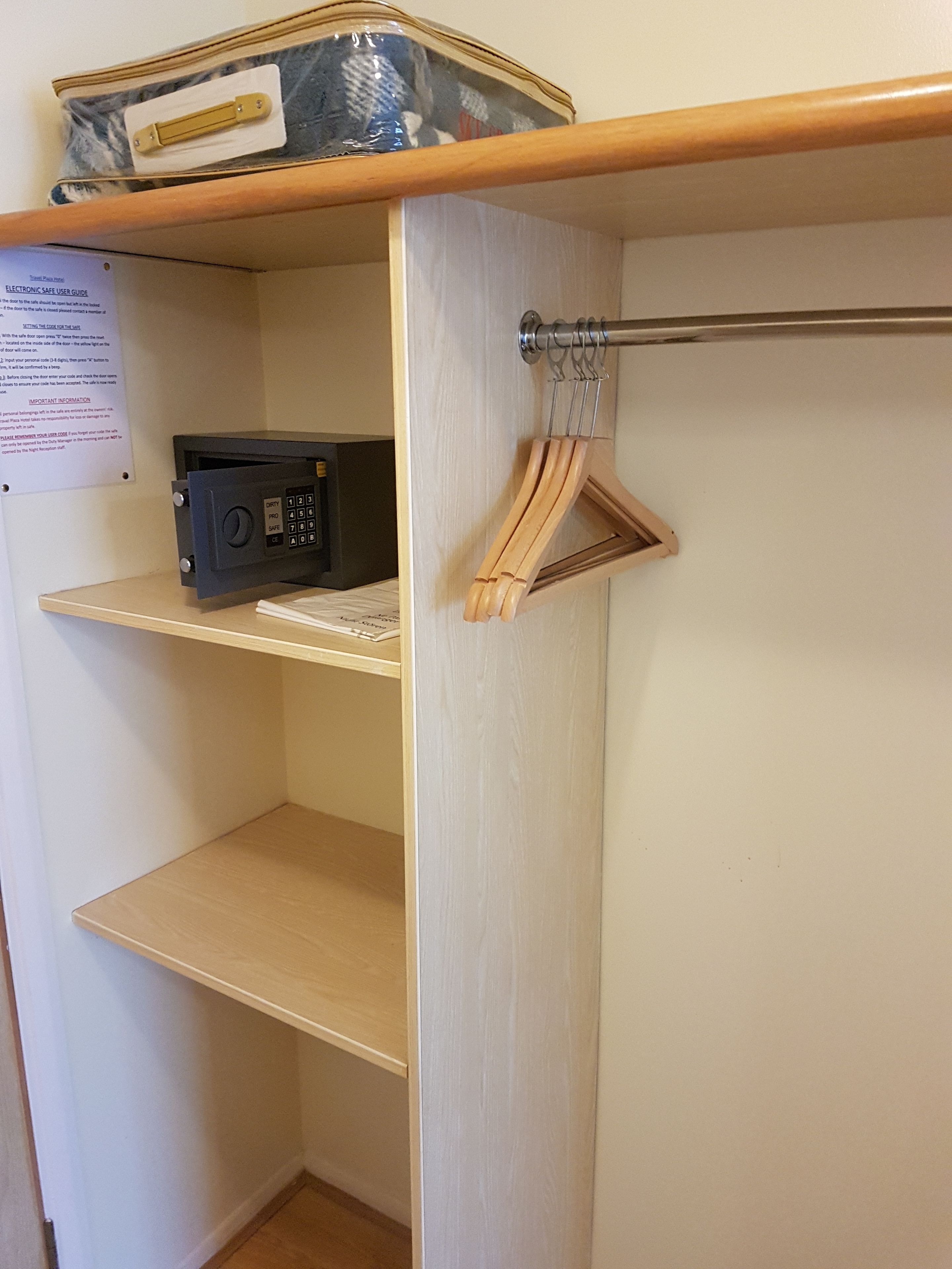 A corner of a room with a wooden shelf, a radio, and a hanging garment rack.