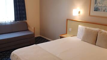 Ett hotellrum med en stor säng, en soffa, ett nattduksbord och en väggmonterad lampa.