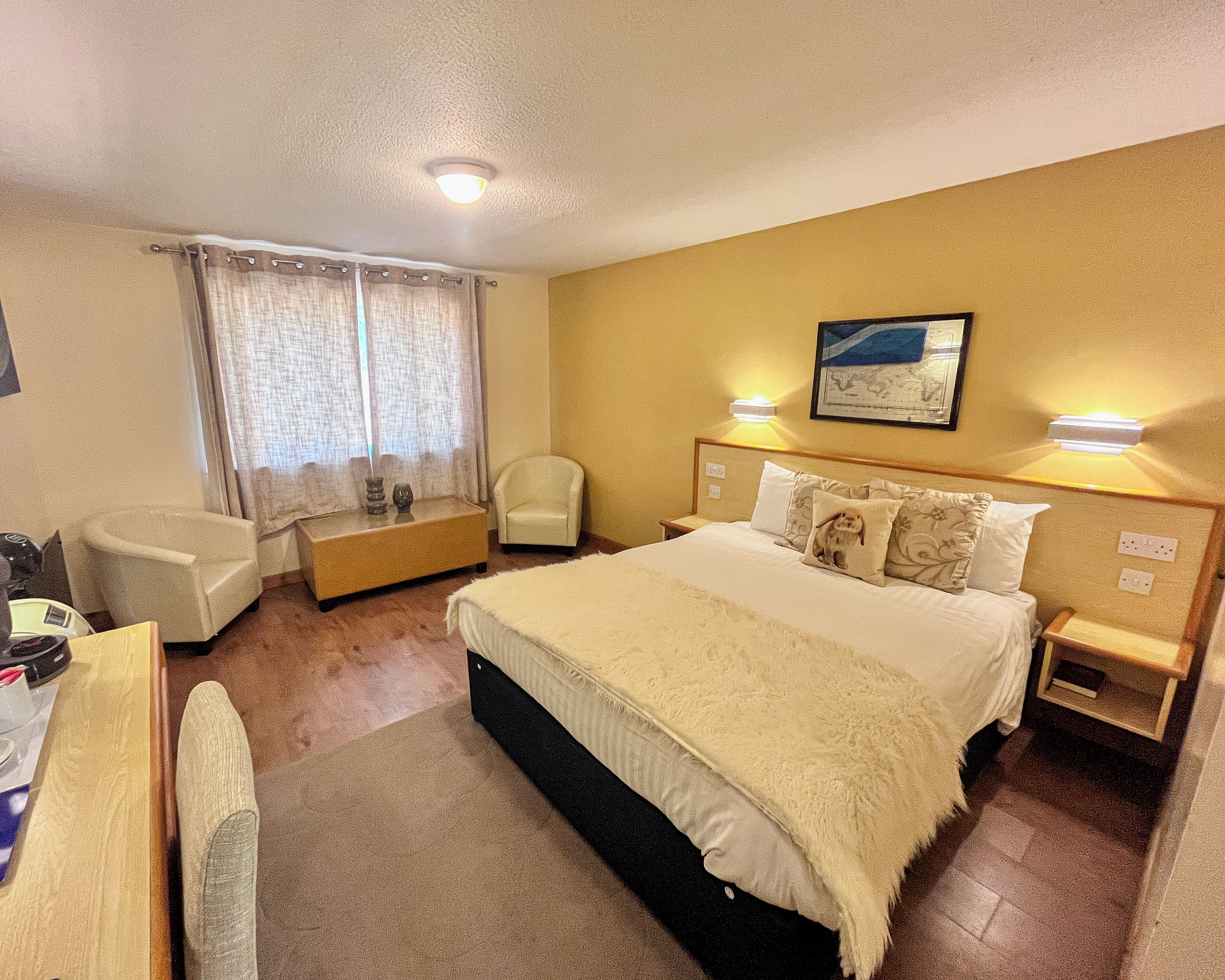 A hotel room with a bed, a chair, a desk, and a window with curtains.