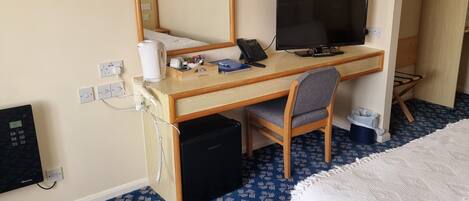 Hotellihuone, jossa on sänky, työpöytä, tietokone, tuoli, pöytälamppu, puhelin, tuuletin ja peili.