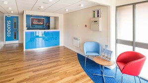 A reception area with a blue counter, a red chair, and a blue chair. - Travelodge Nottingham Trowell M1 (Nottingham)