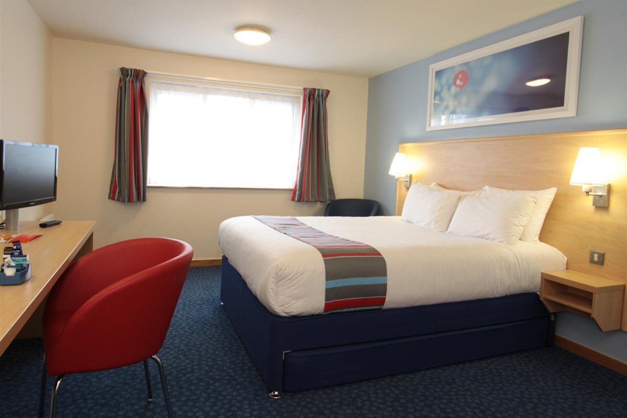 A hotel room with a bed, a desk with a computer, a chair, and a television.