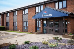 Un hôtel Travelodge avec une façade en briques, un auvent bleu et un parking.